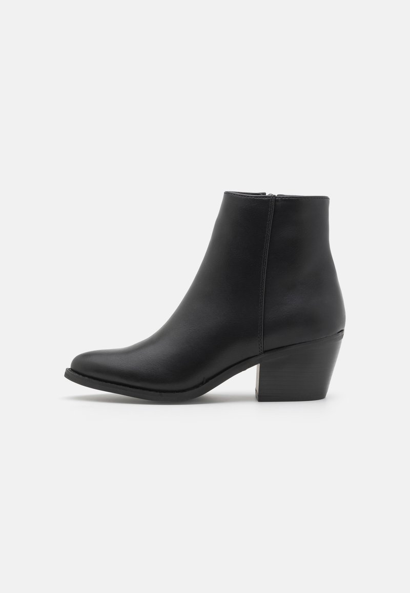 Bottine en cuir noir avec bout pointu, fermeture éclair latérale et talon épais de hauteur moyenne sur fond clair uni.