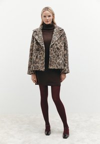 Leopardmuster-Wollmischungsovern mit doppelten Knöpfen, braunem Hochkragenkleid und burgunderfarbenen gerippten Strümpfen, ergänzt durch schwarze High Heels.
