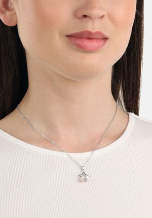 Collana con pendente a forma di stella in argento con dettagli in oro rosa, appesa a una fine catena su una maglia chiara a coste.