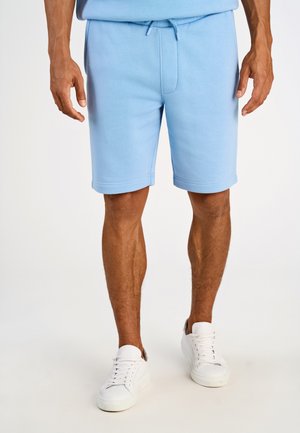 Shorts bleu en mélange de coton avec une taille à cordon, poches latérales et ourlets retroussés, assortis à des baskets blanches sur un fond neutre.
