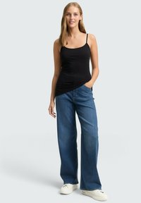 Zwart spaghettihemd gecombineerd met loszittende blauwe jeans en witte sneakers, wat een ontspannen, casual outfit laat zien.