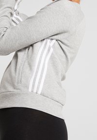 Grå sweatshirt med hvide striber, lavet af blødt materiale. Har en rund halsudskæring og ribbede manchetter, samt en kangaroo lomme.