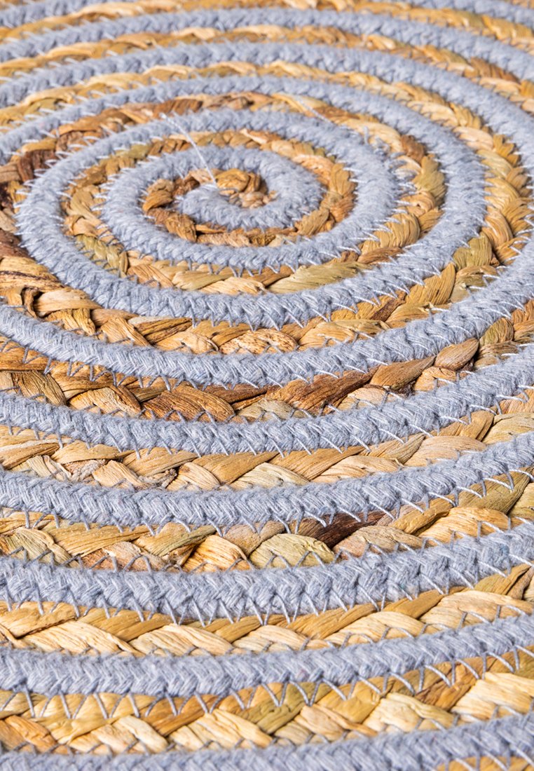 Runder Teppich aus gewebten Naturfasern in Spiralform, mit beigen und grauen Farbtönen, sichtbarer Textur und Nähdetails.