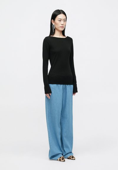 Camisola preta de mangas longas com decote barco, emparelhada com calças de ganga azuis claras de perna larga e sapatos de ponta em padrão de leopardo.