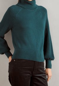 Turquoise turtleneck sweater with textured knit sleeves and ribbed hem. Features voluminous bell sleeves and a fitted bodice.