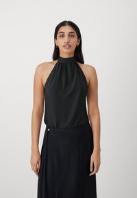 Crni halter top od glatkog materijala s detaljem na izrezanju, uparen s tamnom suknjom sa bočnim kopčanjem.