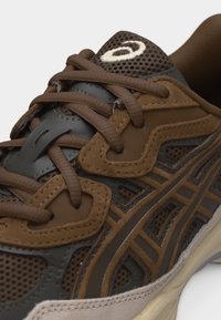 Gros plan sur une chaussure de sport marron et grise avec des panneaux en mesh et en daim, des lacets marron et une semelle en caoutchouc crème.