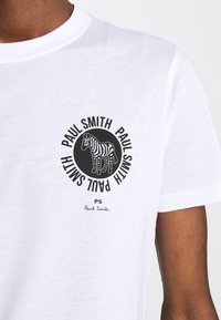 Weißes Baumwoll-T-Shirt mit einem kreisförmigen schwarzen Grafik eines Zebras, umgeben von dem Text "PAUL SMITH" und einer Signatur darunter.