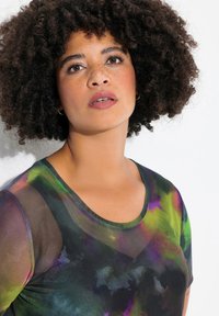 Farverig tie-dye kortærmet top med rund halsudskæring. Materialet er let og gennemsigtigt, med mønstre i grøn, lilla og sort.