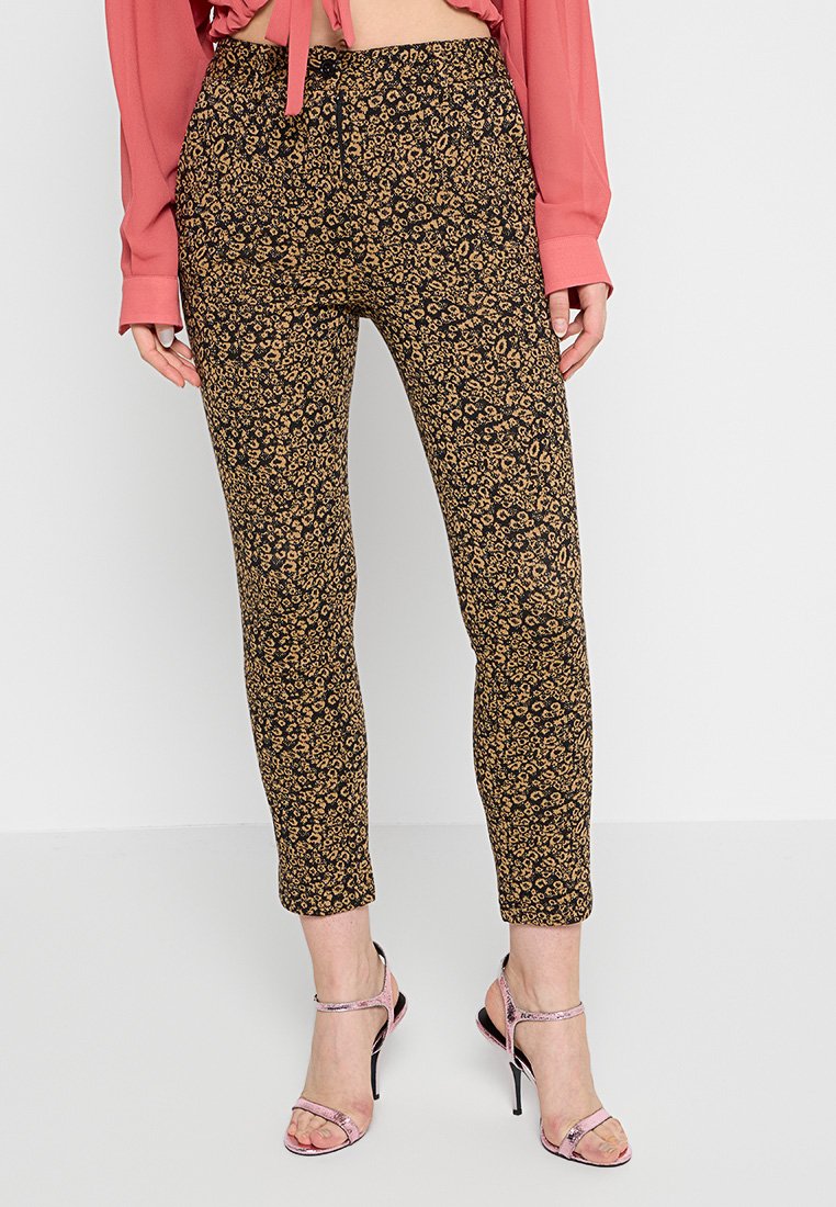 Schwarze und goldene Leopardmuster-Hose, slim fit mit elastischem Bund, knöchellang. Kombiniert mit einer langärmeligen rosa Bluse und Riemchen-Heels.