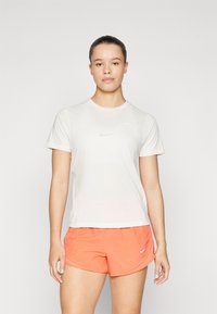 Camiseta deportiva blanca de manga corta con un logo reflectante, combinada con pantalones cortos de color naranja brillante que presentan un sutil logo de Nike.