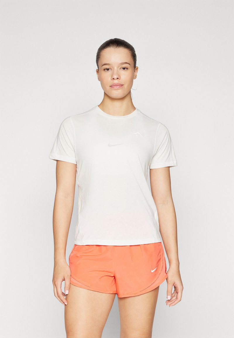 Valge sportlik T-särk lühikeste varrukatega ja peegeldava logoga, kokku sobitatud heledate oranžide lühikesed püksid, millel on õrn Nike logo.