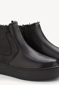 Schwarze Leder-Ankle-Boots mit glatter Textur, seitlichen Reißverschlüssen, einer flachen schwarzen Gummisohle und einem weichen Futter aus Fell oben.