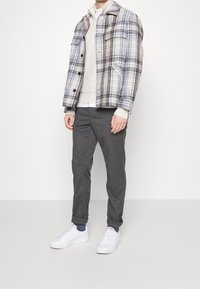 Plaid jacket in blue and brown, light sweater, gray pants, and white sneakers; features pockets, button closures, and rolled cuffs.