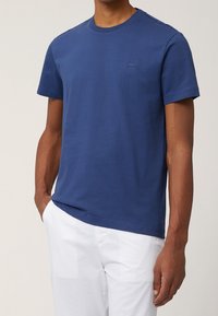 Marineblå bomuld t-shirt med rund halsudskæring, korte ærmer og et lille logo på brystet, kombineret med hvide bukser.