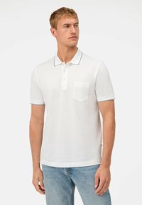 Witte polo shirt van katoen, met een kraag met een marineblauwe accent, korte mouwen en een borstzak. Gestyled met lichtblauwe jeans.