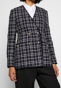 Mörkblå rutigt kavaj i texturerat tyg, med dubbelknäppt design och guldfärgade knappar samt fickor. Strukturerad passform.