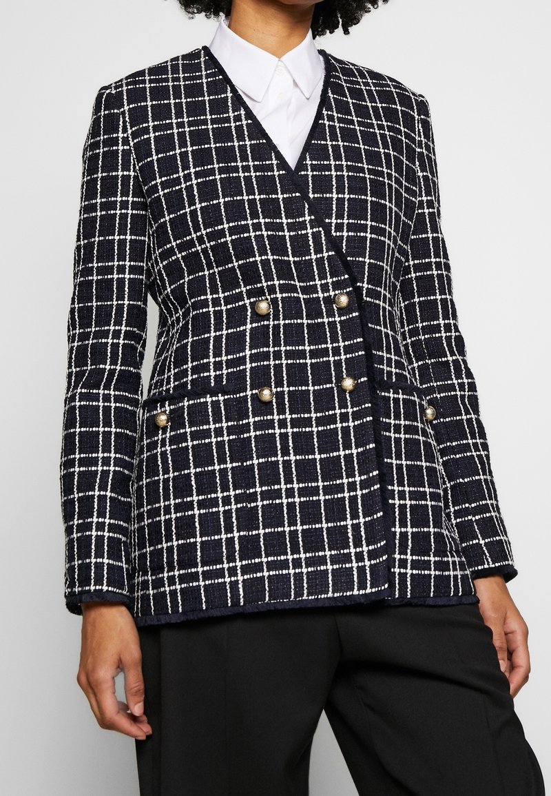 Mörkblå rutigt kavaj i texturerat tyg, med dubbelknäppt design och guldfärgade knappar samt fickor. Strukturerad passform.