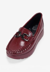 Scarpa slip-on in pelle bordeaux con finitura texturizzata, caratterizzata da un accento di catena argentata e una suola spessa, progettata per il comfort.