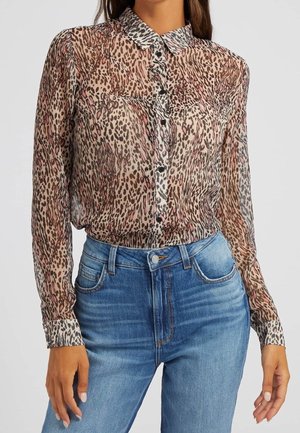 Hun har en gennemsigtig, langærmet, knappet bluse med dyreprint og højttaljede blå jeans på.