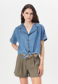 Korta ärm, kort croppad denimskjorta med krage, knappstängning och knyt framtill. Bärs över olivgröna, veckade shorts. Slät textur.