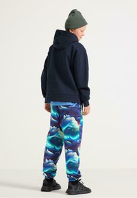 Granatowa bluza z kapturem, kolorowe spodnie dresowe w kwiatowy wzór, zielona czapka i czarne trampki. Codzienne ubranie na chłodną pogodę.