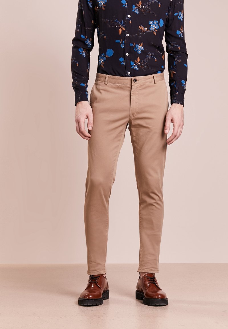 Beige kalhoty slim-fit vyrobené z bavlněné směsi se zapínáním na knoflík a předními kapsami, doplněné hnědými koženými šněrovacími botami.