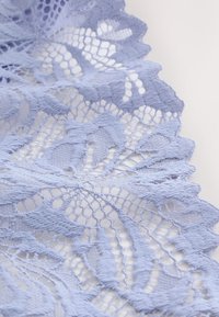 Lyseblåt blonde stof med blomstermønstre og bladmønstre, prydet med bølgekantede kanter og indviklede åbenarbejdsdetaljer på en hvid baggrund.