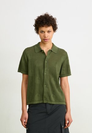 Olive green short-sleeve shirt in textured knit, featuring a collared neckline and button closure, with a subtle pattern throughout.