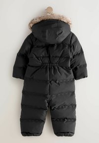Schwarzer gepolsterter Kinder-Schneanzug mit elastischem Bund und einer mit Fell besetzten Kapuze, die an einem Holzpflock hängt.