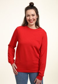 Felpa rossa con maniche lunghe, collo tondo e una texture liscia. Abbinata a jeans blu, caratterizzati da una vestibilità comoda e polsini a costine.