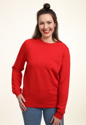Felpa rossa con maniche lunghe, collo tondo e una texture liscia. Abbinata a jeans blu, caratterizzati da una vestibilità comoda e polsini a costine.