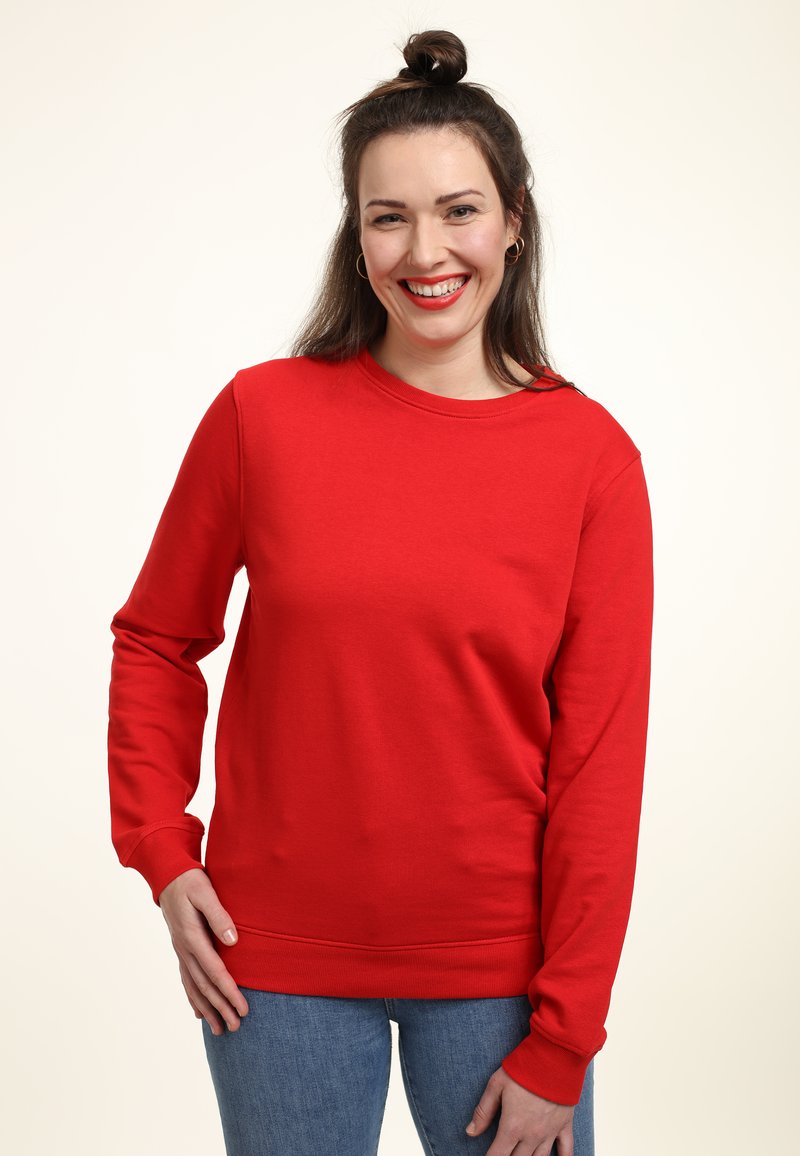 Felpa rossa con maniche lunghe, collo tondo e una texture liscia. Abbinata a jeans blu, caratterizzati da una vestibilità comoda e polsini a costine.