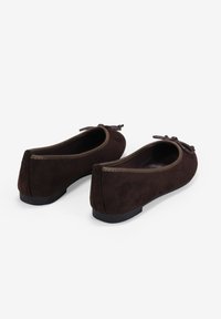 Bailarinas de ante marrón con suela plana y detalle de lazo en la parte delantera. Los bordes están bordeados con un ribete en contraste.