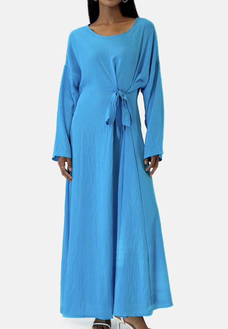 Lyseblå maxikjole med lange ærmer, rund halsudskæring og bindedetalje i taljen. Fremstillet af blødt, tekstureret stof.