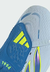Gros plan sur une chaussure de sport blanche et bleue avec un logo Adidas jaune néon, des accents violets et le texte « NANOSTRIKE » sur le matériau supérieur.