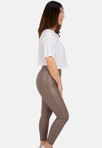 Leggings en simili cuir marron assortis à un t-shirt blanc court. Les leggings présentent des détails de couture et une texture lisse.