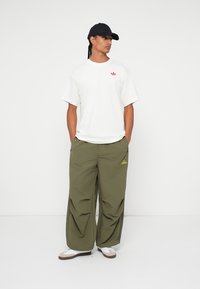 Hvit kortermet t-skjorte med en rød logo, olivengrønne cargo-bukser med en Adidas-logo, og en svart caps. Antrekket har en avslappet, oversized passform.