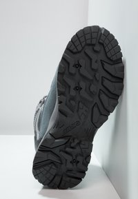 Suela de zapato de senderismo gris con un patrón texturizado y una suela de goma negra resistente. Presenta surcos y tacos profundos para tracción en diversas superficies.