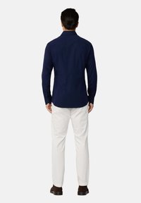 Camisa de botones de manga larga en color navy con una textura suave, ajuste ceñido y dobladillo redondeado, combinada con pantalones de color claro y zapatos marrones.