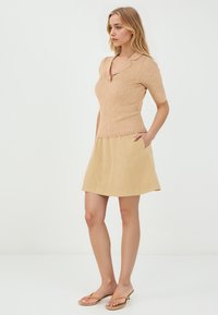 Haut beige à manches courtes en maille côtelée avec col et détails de boutons, associé à une jupe d'été beige clair en forme de A avec poches latérales.