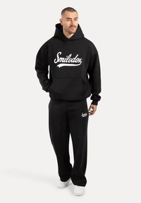 Sudadera negra con el logo "Smilodox" en blanco, combinada con pantalones de chándal negros a juego. Tela suave y corte relajado para mayor comodidad.