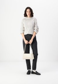 Svetlo sivi pleteni pulover z teksturiranim vzorcem, v kombinaciji z črnimi kavbojkami in krema barvo torbico. Model nosi črne loaferje.
