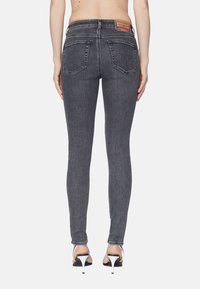 Jeans de denim gris ajustados con cintura alta, dos bolsillos traseros y una etiqueta de cuero de marca. Tejido texturizado con un sutil patrón deslavado.