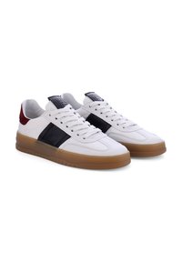 Witte leren sneakers met zwarte zijstrepen en rode accenten op de hak. Voorzien van een rubberen zool en vetersluiting. Geribbeld detail op de tong.
