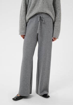 Personne portant un pantalon en maille gris à jambes larges avec taille à cordon et des ballerines noires pointues, associé à un pull gris ample.