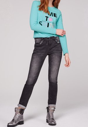 Türkises Langarmshirt mit schwarzem und pinkem Text; schwarze Skinny Jeans; graue Kampfstiefel mit silbernen Akzenten und aufgerollten Säumen.
