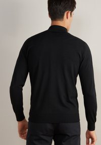 Svart långärmad tröja med hög krage, tillverkad av ett mjukt stickat material. Har ribbade muddar och nederkant samt figurnära design.