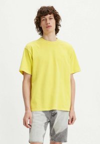 Yellow cotton t-shirt with a crew neckline, short sleeves, and a relaxed fit, paired with light grey shorts featuring a faded pattern.