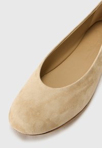 Ballet flat de ante beige, con punta redondeada, textura suave, costuras mínimas, forro interior suave y suela delgada.